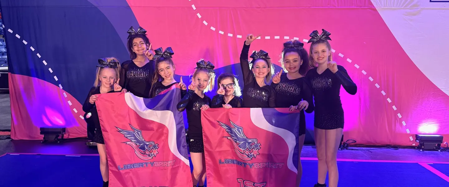 8 cheerleaders holding up their 1st place flag for the Liberty Spirit Grand Champion in excitement