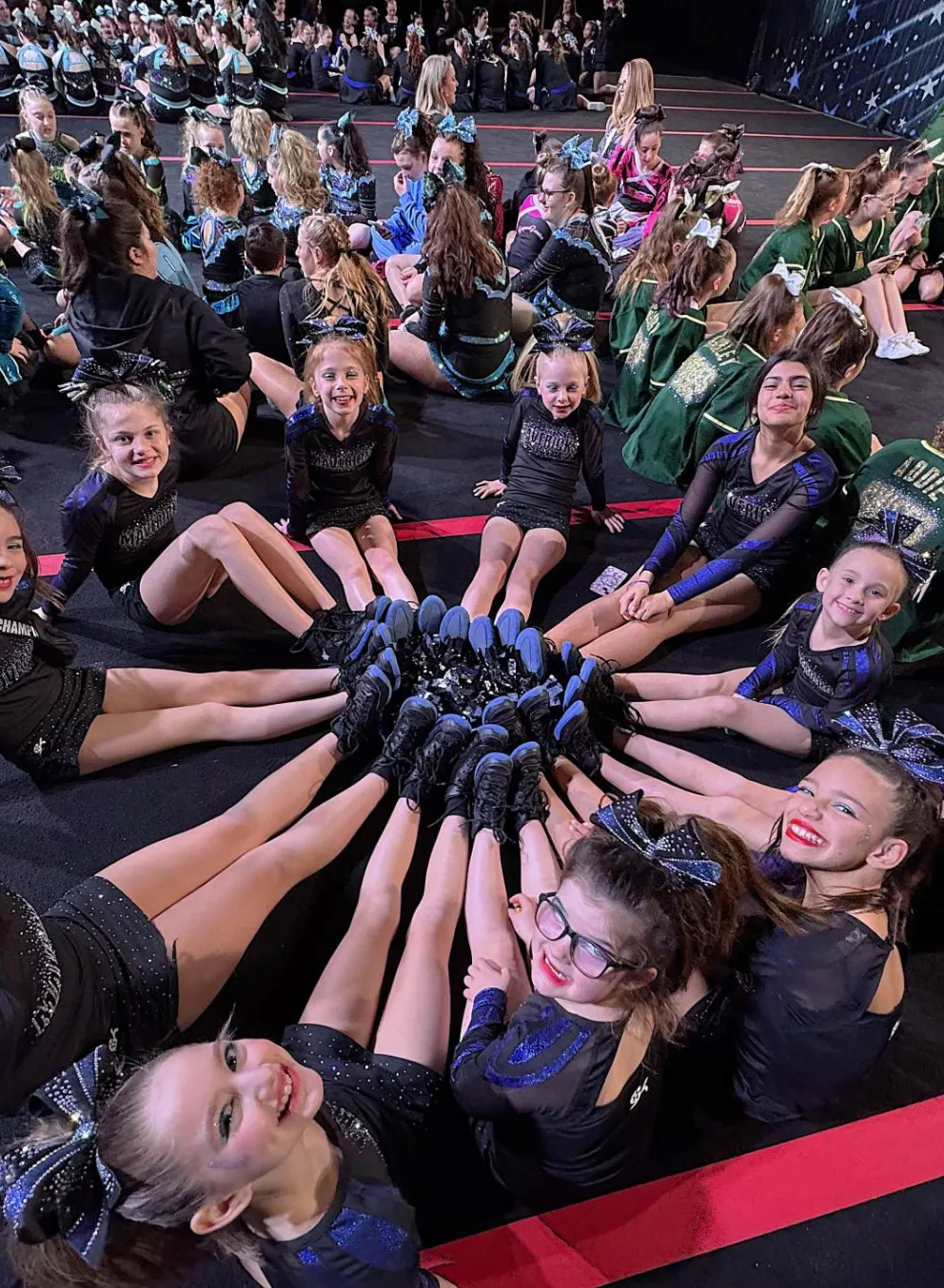Group of 11 cheer leaders making a circle with legs in the middle smiling at the camera