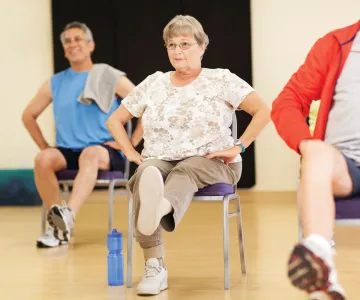 Active older woman on a chair getting a workout in with other male participants in the background