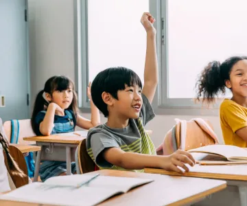 Group of happy kids in a classroom raising their hand waiting to be call on