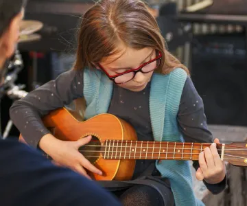 Music teacher teaching guitar and ukulele to little daughter