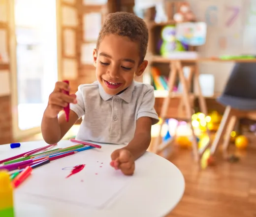 Beautiful african american toddler drawing using paper and marker pen smiling at kindergarten