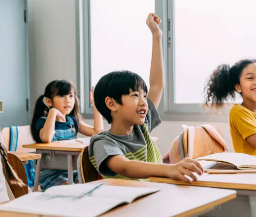 Group of happy kids in a classroom raising their hand waiting to be call on