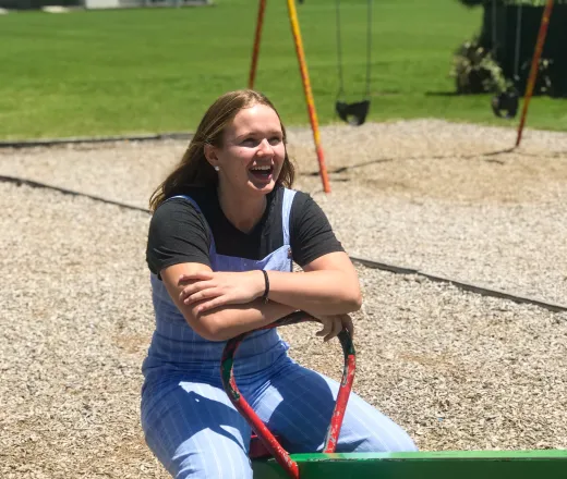 Smiling teenage girl sitting on a teeter totter outside on a playground